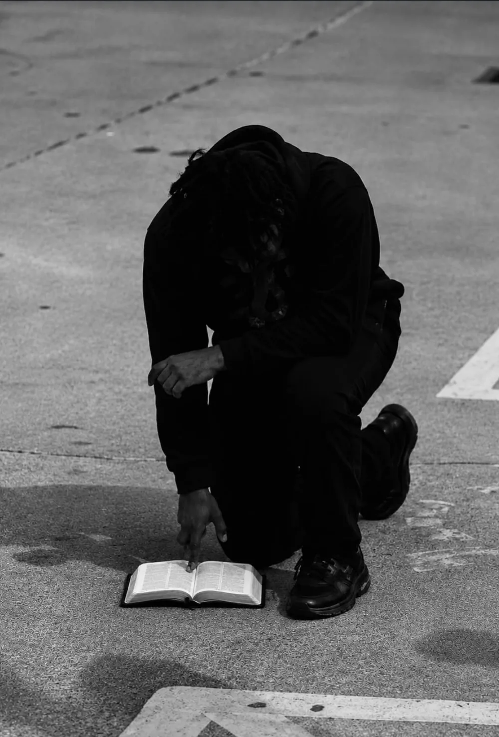 Minister Dom Patterson kneeling on the pavement, pointing to an open Bible