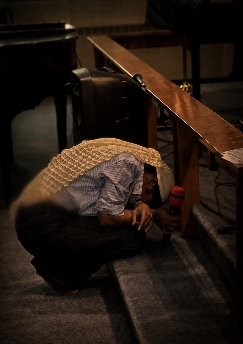 A man kneels in prayer at the altar rail, head bowed beneath a prayer shawl