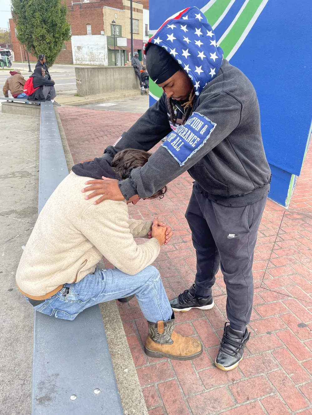 A GNP member lays a hand on a man's shoulder and prays with him on a city sidewalk during street outreach